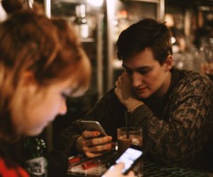 Two people look at smartphones while seated at a café table