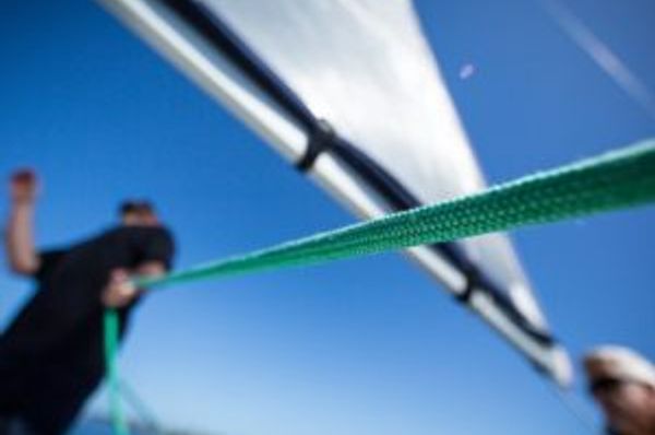Taut green rope crosses a blurred low-angle view of two people and a sail