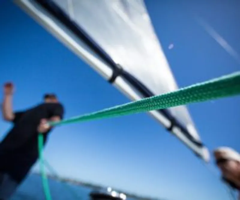 Taut green rope crosses a blurred low-angle view of two people and a sail