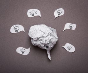 Crumpled paper shaped like a brain surrounded by speech bubbles with light bulbs