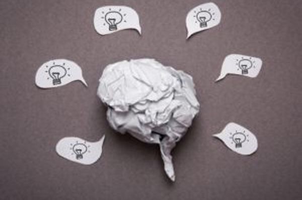 Crumpled paper shaped like a brain surrounded by speech bubbles with light bulbs
