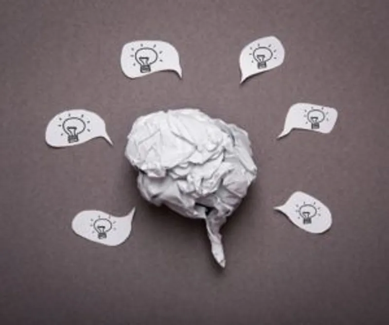 Crumpled paper shaped like a brain surrounded by speech bubbles with light bulbs
