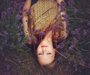 Person lies with eyes closed among purple flowers