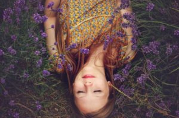 Person lies with eyes closed among purple flowers
