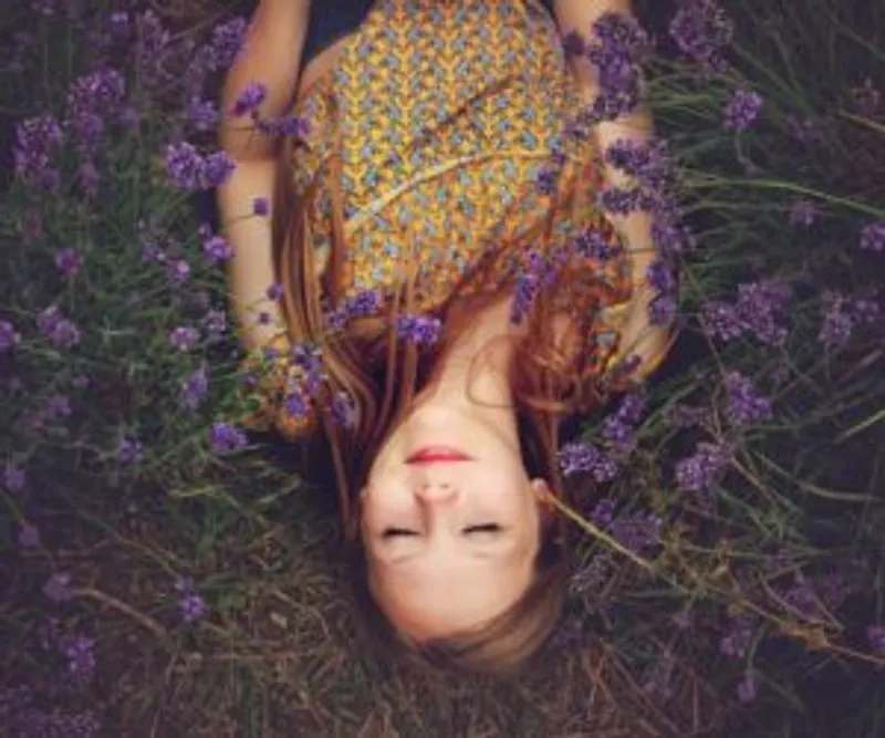 Person lies with eyes closed among purple flowers