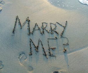 Marry me? traced in wet sand beside foamy seawater
