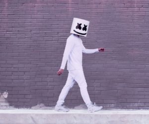 Person in white walking beside a brick wall with a smiling cube helmet