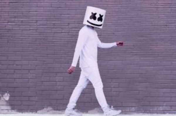 Person in white walking beside a brick wall with a smiling cube helmet