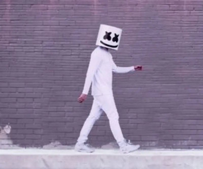 Person in white walking beside a brick wall with a smiling cube helmet