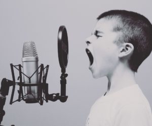 Child with mouth open facing a studio microphone and circular pop filter