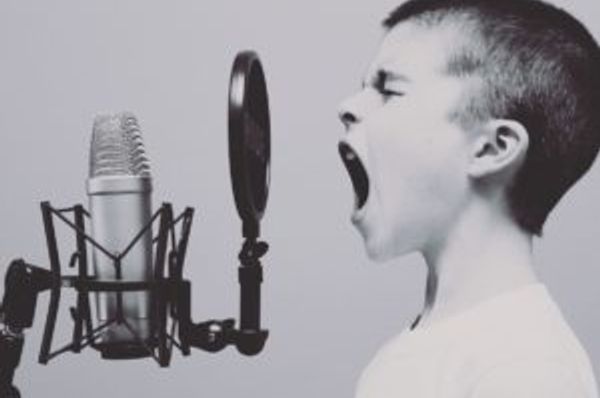 Child with mouth open facing a studio microphone and circular pop filter
