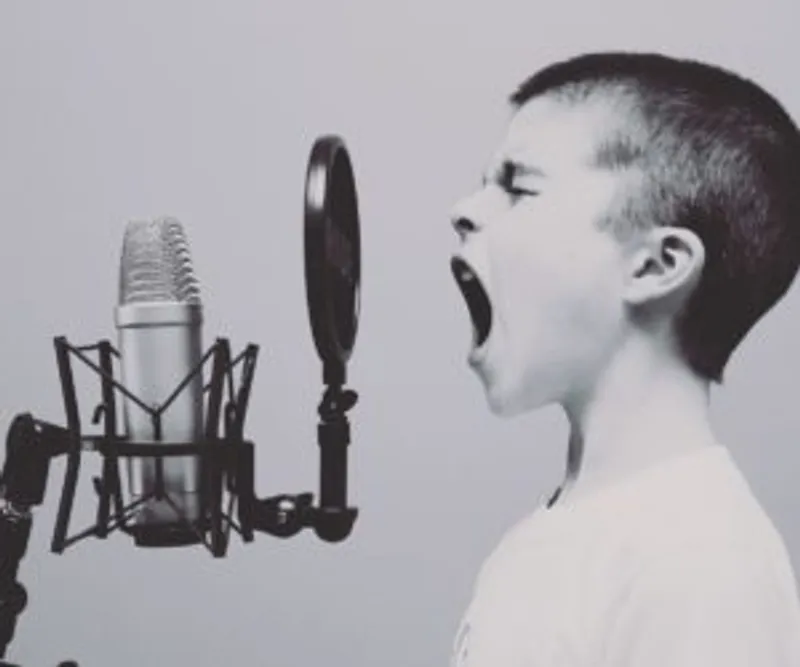 Child with mouth open facing a studio microphone and circular pop filter