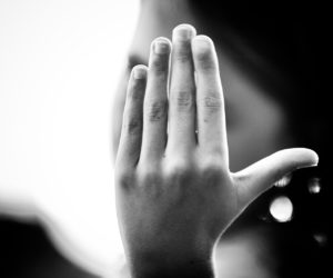 Raised hand blocking a blurred face in a black-and-white scene