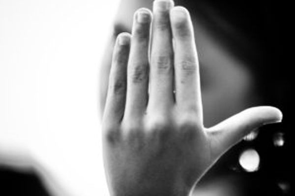 Raised hand blocking a blurred face in a black-and-white scene