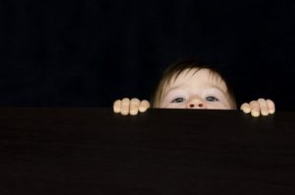 Face and hands peeking over a dark surface against a black background