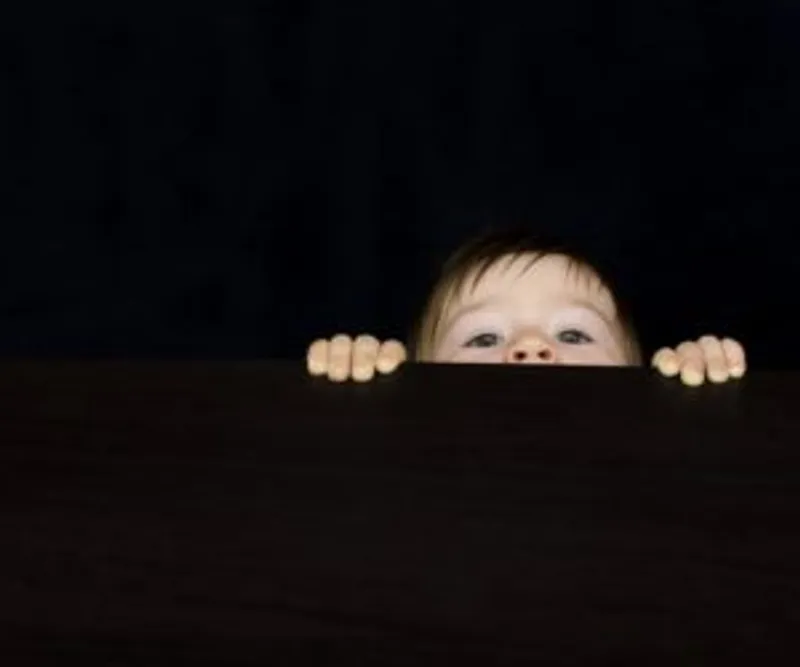 Face and hands peeking over a dark surface against a black background