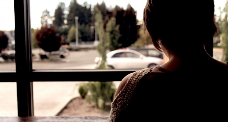 Person seen from behind beside a large window, with a car outside