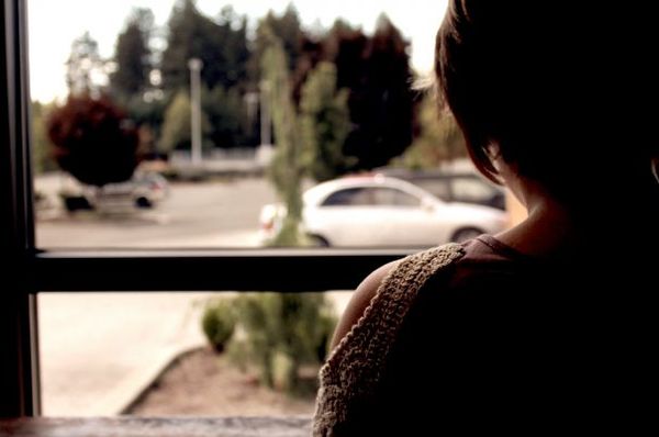 Person seen from behind beside a large window, with a car outside