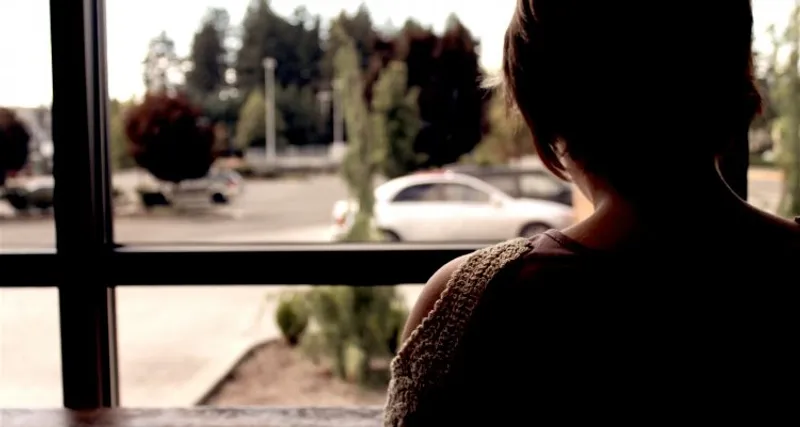Person seen from behind beside a large window, with a car outside
