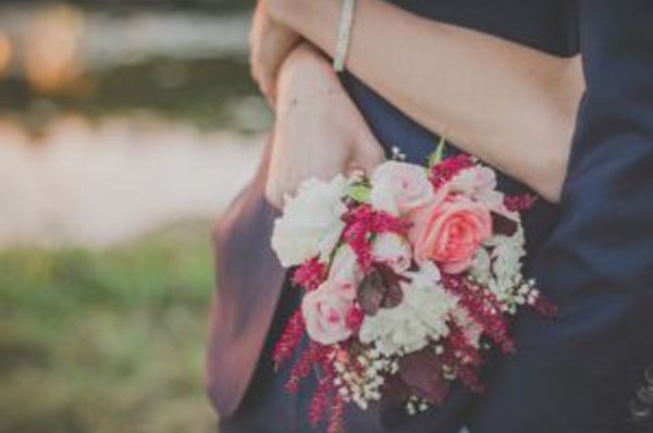 Two people embrace while one holds a bouquet behind the other