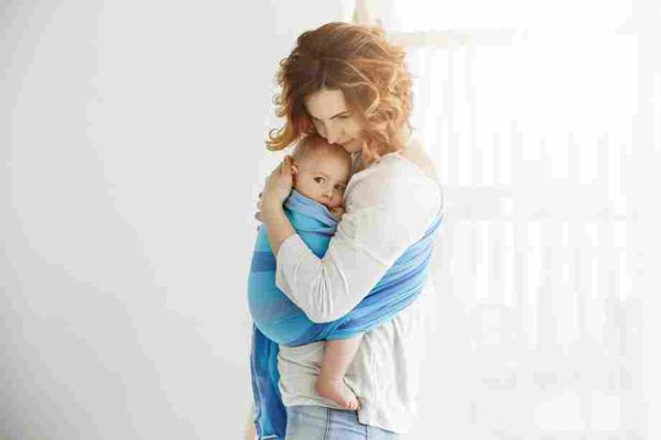 Adult holding an infant close in a blue fabric sling