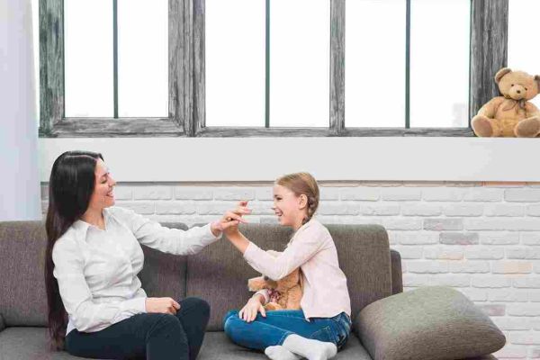 Adult and child sit on a sofa, smiling and touching hands