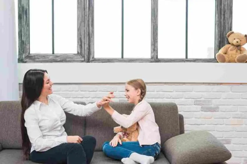 Adult and child sit on a sofa, smiling and touching hands