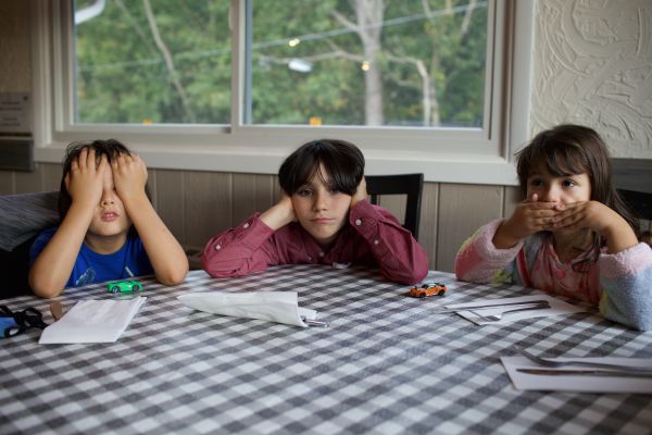 Three children at a table cover their eyes, ears, and mouth
