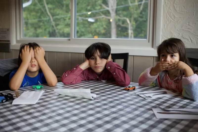 Three children at a table cover their eyes, ears, and mouth