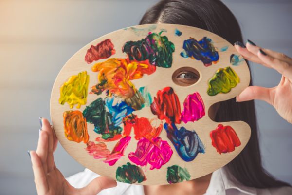 Person holds a paint-covered artist palette in front of their face