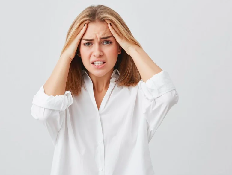 Person in a white shirt pressing both hands against their temples