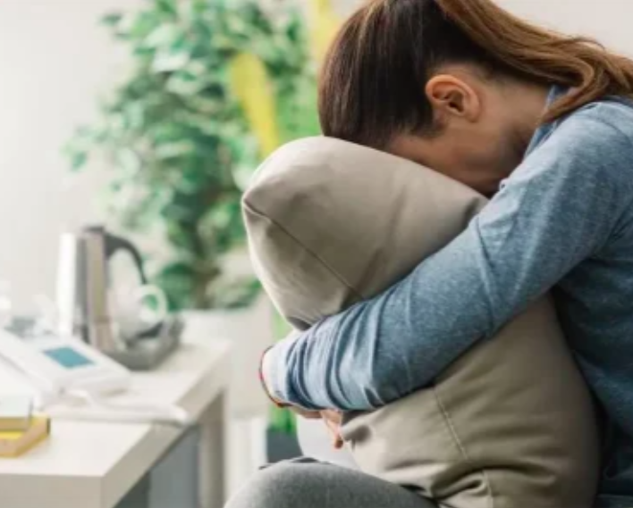 Seated person hugging their knees with their face lowered against them