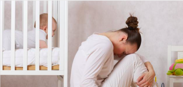 Person curled up on the floor beside a crib with a baby inside