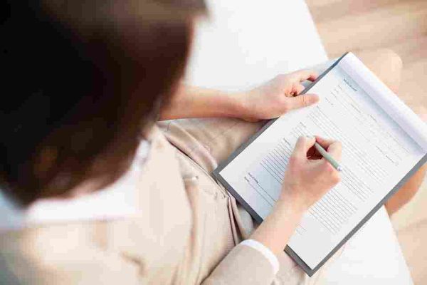 Person writing on a form attached to a clipboard