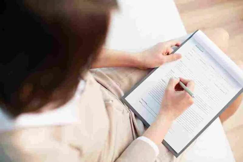 Person writing on a form attached to a clipboard