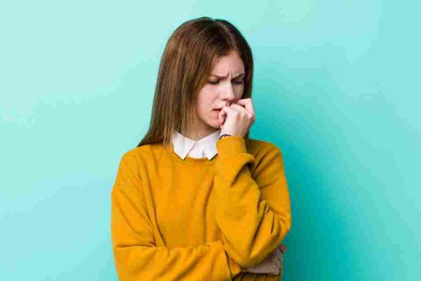 Person in a yellow sweater bites a fingernail against a plain wall
