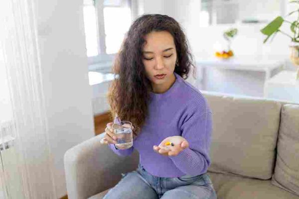 Seated adult holds a glass of water and pills in an open hand