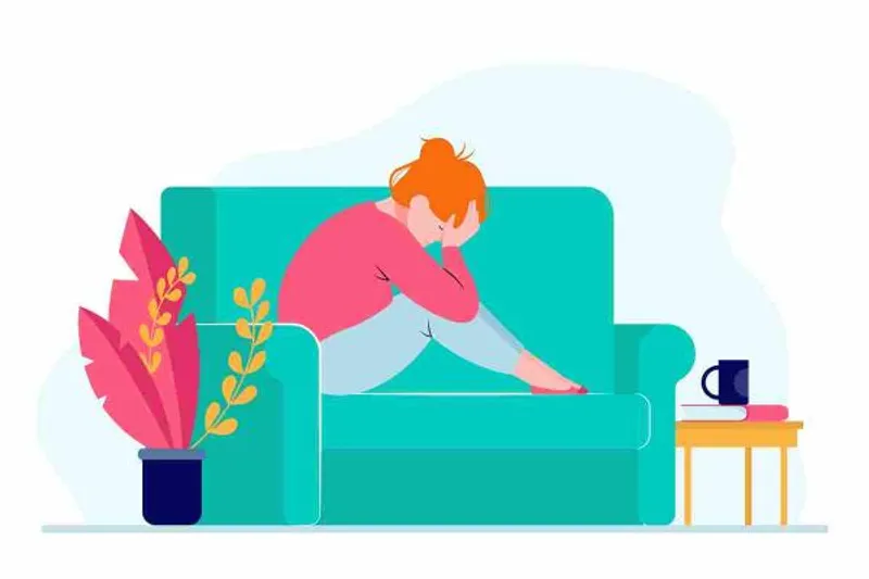 Person sitting curled up on a sofa with their head resting in one hand