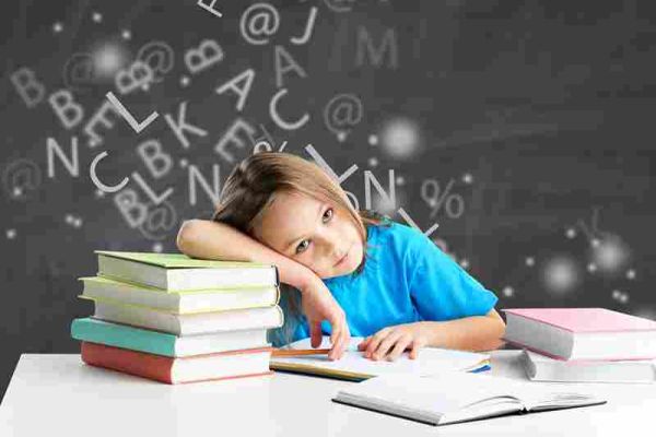Child rests their head on a stack of books at a desk with letters in the background