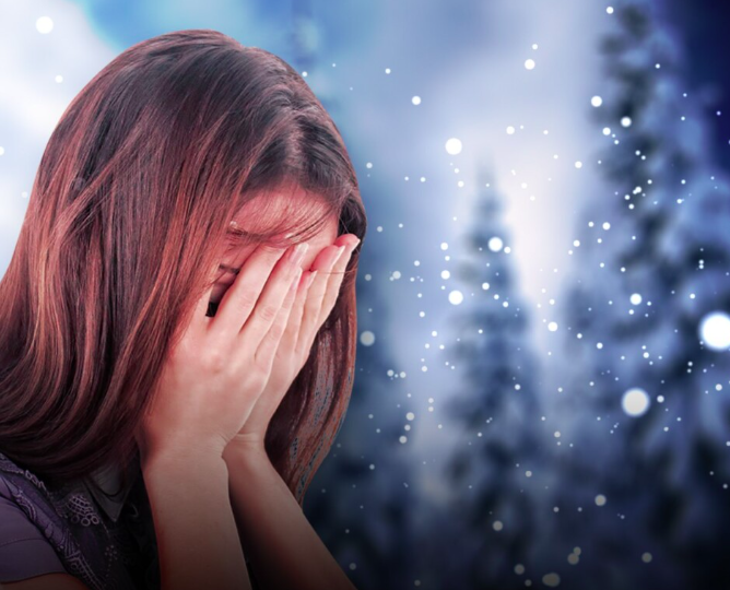 Person covering their face with both hands against a snowy forest backdrop