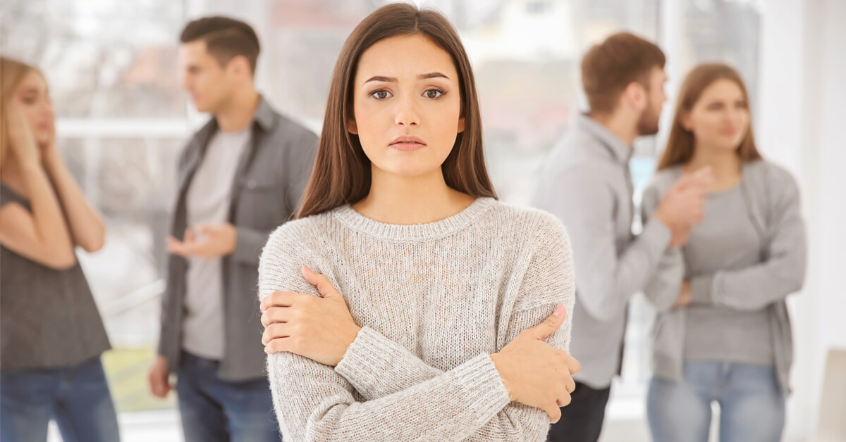 Person standing with arms folded while blurred groups talk in the background