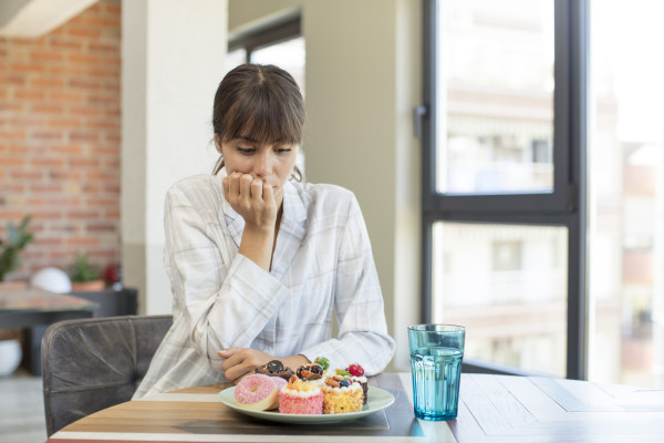 Seated person looks down at a plate of pastries with a hand near their mouth