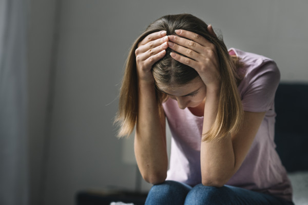 Person sits leaning forward with both hands on their head