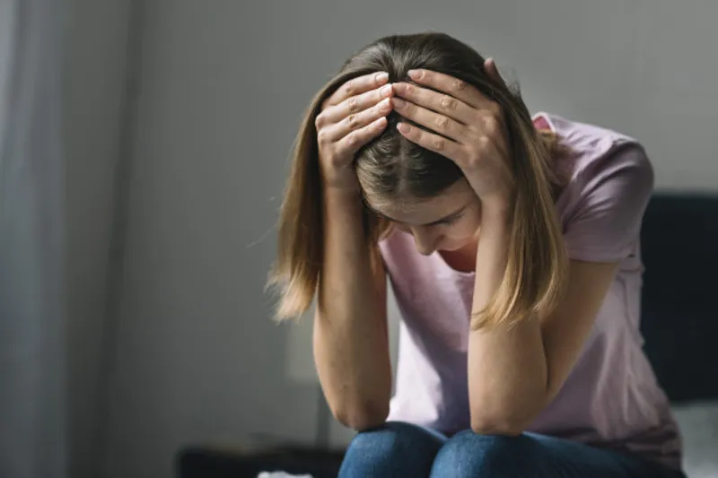 Person sits leaning forward with both hands on their head