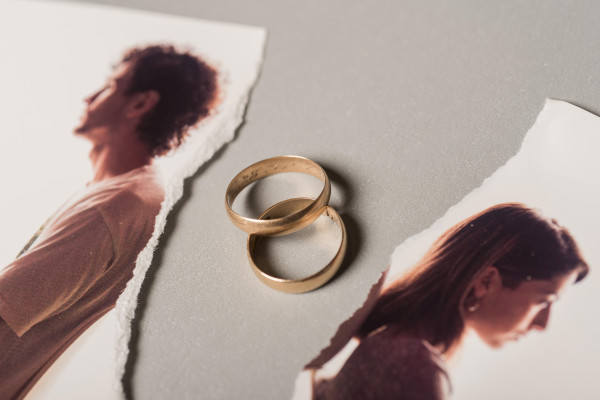 Two gold rings lie between torn portraits of two people