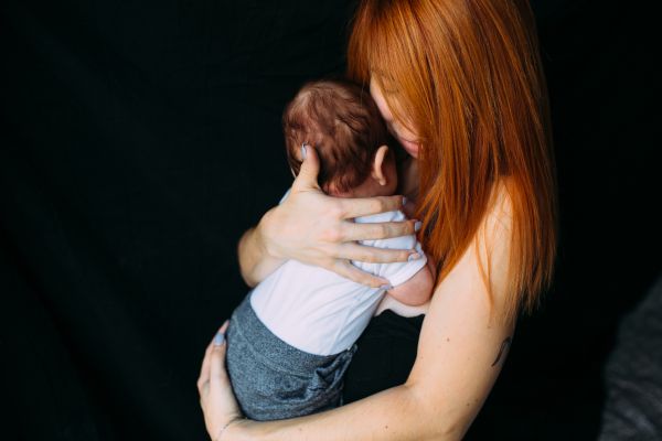 Red-haired adult holds a baby close against a black background