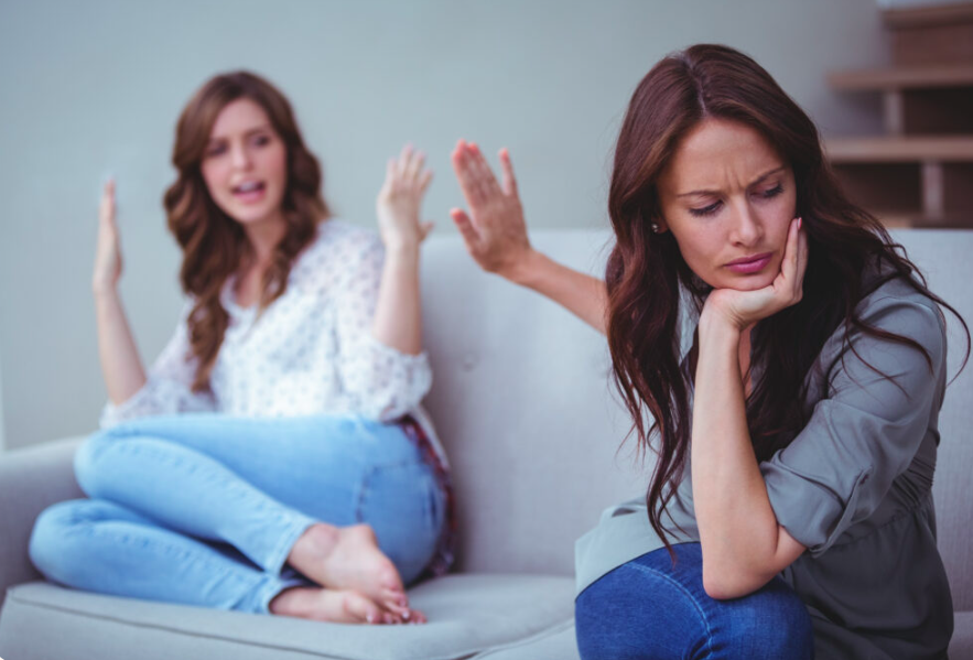 One person rests their chin on a hand while another gestures from the sofa