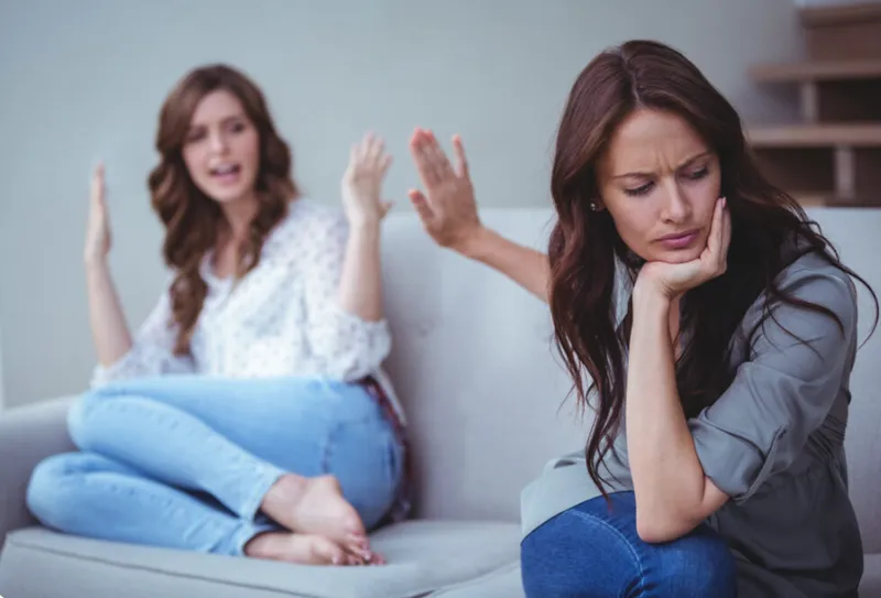 One person rests their chin on a hand while another gestures from the sofa