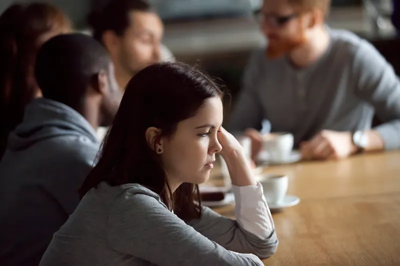 Person sits at a café table with several people blurred in the background