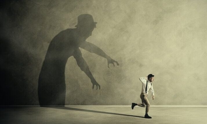Small running figure moves away from a large reaching shadow on a wall